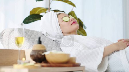 Téléchargez les photos : Belle femme portant une serviette sur la tête posée sur le lit du spa se détendre avec des tranches de concombre sur les yeux à la salle de spa. Concept d'aromathérapie Spa - en image libre de droit