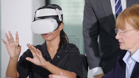 Téléchargez les photos : Femme d'affaires en lunettes de réalité virtuelle et les mains levées travaillant avec l'équipe d'affaires dans la salle de réunion au bureau moderne. Concept de simulation et métaverse - en image libre de droit