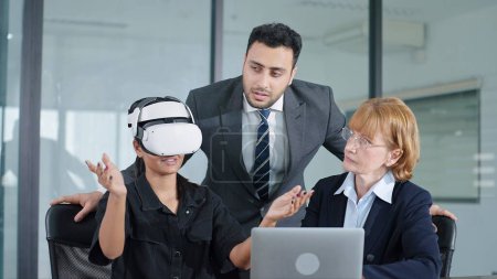 Téléchargez les photos : Jeune femme testant des lunettes VR ou des lunettes de travail avec deux collègues. Équipe d'affaires de trois personnes travaillant sur la réalité virtuelle dans la salle de réunion du bureau moderne. Rencontre avec la technologie - en image libre de droit