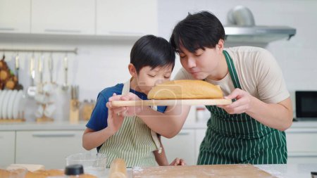 Photo for Father and son baker wearing apron sniffing aroma from bread after baked. Enjoy smelling fresh bread. Food and cuisine concept, Happy asian family - Royalty Free Image