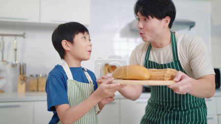 Téléchargez les photos : Heureuse famille asiatique, père et fils aiment s'entraider pour cuisiner du pain fait maison, passer du temps en vacances ensemble dans la cuisine à la maison - en image libre de droit