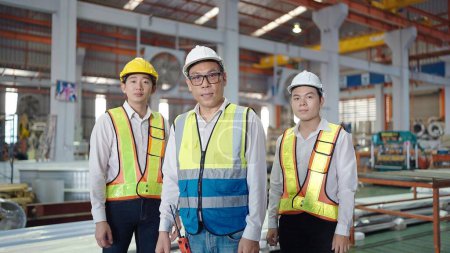 Téléchargez les photos : Ingénieurs asiatiques confiants portant casque de sécurité et gilet debout à l'usine industrielle. Trois ingénieurs professionnels hommes regardant la caméra tout en étant debout à l'usine. Concept de travail d'équipe - en image libre de droit