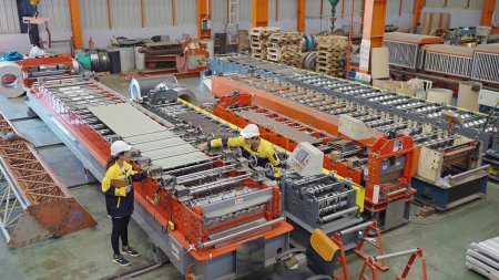 Téléchargez les photos : Ingénieurs industriels hommes montrant le processus des machines pour produire le toit de tôle aux femmes directeur dans l'usine de fabrication de métaux - en image libre de droit