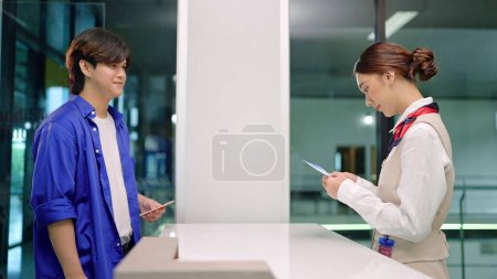 Photo for Young Asian women ground staff checking boarding pass and ticket of passenger before taking flight at airline counter in airport. Airplane travel and transportation - Royalty Free Image