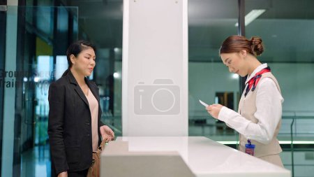 Photo for Young Asian women ground staff checking boarding pass and ticket of passenger before taking flight at airline counter in airport. Airplane travel and transportation - Royalty Free Image