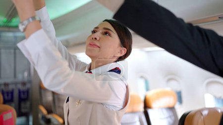 Téléchargez les photos : Des hôtesses de l'air asiatiques en uniforme fermant le compartiment à bagages supérieur dans l'avion. Enregistrement du coffre à bagages aérien avant le décollage de l'avion - en image libre de droit