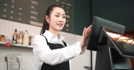 Téléchargez les photos : Femme barista ou propriétaire dans tablier à l'aide de l'ordinateur prendre commande auprès du client dans le café. Concept d'entreprise du café - en image libre de droit