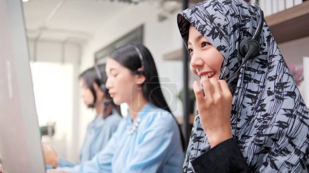Foto de Hermosa mujer musulmana operador de centro de llamadas que trabaja en la computadora en la oficina. Mujeres musulmanas con auriculares usando computadora mientras asesoran en el centro de llamadas - Imagen libre de derechos