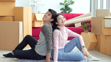 Téléchargez les photos : Heureux jeune couple asiatique assis sur le sol dans le salon se sentant bien de déménager vers une nouvelle maison et la planification de la nouvelle conception de la maison - en image libre de droit