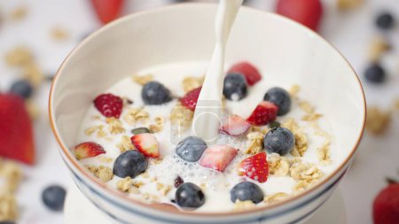 Foto de Leche vertiendo en un tazón de desayuno saludable crujiente Granola Cereales con fresa, comida vegana de arándanos, comer limpio, concepto de dieta - Imagen libre de derechos