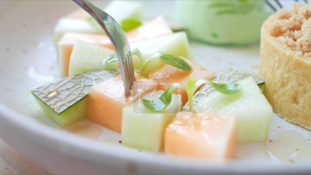 Photo for Close up A fork dipped into slice of cantaloupe, melon on dish which is rich in vitamins and minerals. Eating fruits for healthcare concept - Royalty Free Image