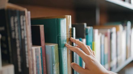 Téléchargez les photos : Fermez la recherche de livres sur les étagères de la bibliothèque. Sélectionnez un livre sur étagère. Etudier l'éducation au savoir en librairie - en image libre de droit
