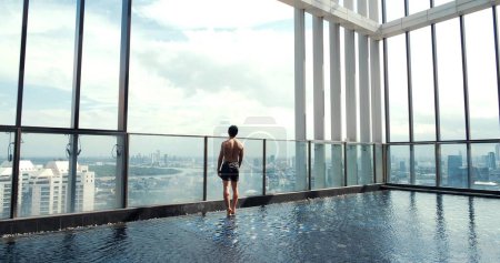 Foto de Vista trasera del hombre joven de pie en la piscina mirando a la hermosa vista y el cielo azul en el día - Imagen libre de derechos