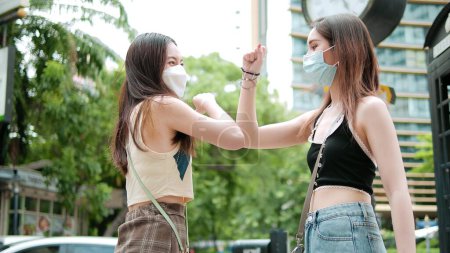 Photo for Two beautiful young asian woman best friend wearing protective face masks greeting elbow bumps to prevent infection at city street outdoors - Royalty Free Image
