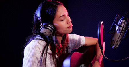 Photo for Young asian woman artist singing song at music studio. Woman singer wearing headphones using microphone singing a song in recording neon studio - Royalty Free Image