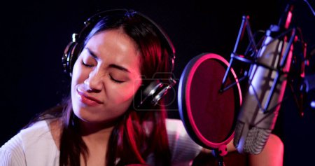 Photo for Happy young asian woman wearing headphones playing guitar acoustic recording in studio. Woman performing guitar acoustic solo intro - Royalty Free Image