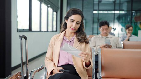Photo for Young hispanic latin woman passenger checking depature boarding pass while sitting on chair in terminal departure gate waiting flight at international airport - Royalty Free Image
