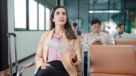 Téléchargez les photos : Jeune femme hispanique latine vérifiant la carte d'embarquement de la dépouille alors qu'elle était assise sur la chaise à la porte d'embarquement terminal en attente d'un vol à l'aéroport international - en image libre de droit