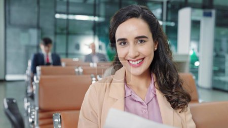Foto de Rostro sonriente de jóvenes pasajeras latinas hispanas sentadas en la puerta terminal del aeropuerto mientras esperan el vuelo del avión mirando a la cámara. Concepto de viaje - Imagen libre de derechos