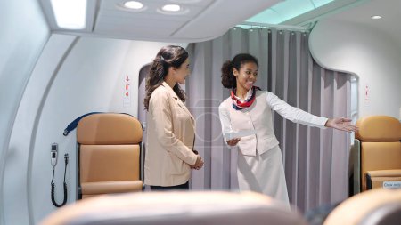 Téléchargez les photos : Les jeunes femmes hôtesses de l'air, hôtesse de l'air en uniforme debout à l'entrée de l'avion, souriaient amicalement, vérifiaient la carte d'embarquement des passagers et accueillaient les passagers. Transport aérien - en image libre de droit