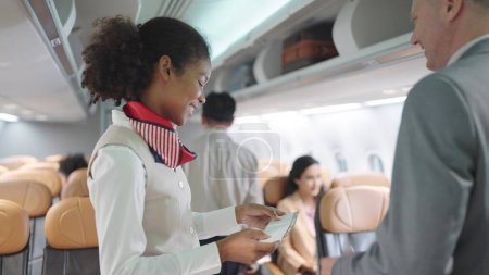 Téléchargez les photos : Les hôtesses de l'air accueillent les passagers à bord de l'avion et vérifient la carte d'embarquement des passagers accueillant le vol. Transport aérien - en image libre de droit