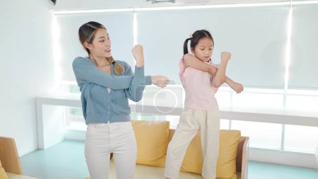 Foto de Madre asiática enseñando ejercicios de hija pequeña juntos en la mañana del fin de semana. La madre y la hija activas se dedican a ejercicios en casa. Concepto de relación madre e hijo - Imagen libre de derechos