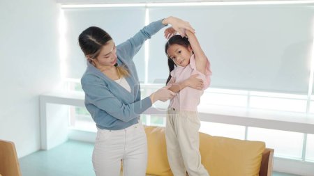 Téléchargez les photos : Mère asiatique enseignant des exercices de petite fille ensemble le matin le week-end. Mère et fille actives sont engagées dans des exercices à la maison. Concept de relation mère-enfant - en image libre de droit