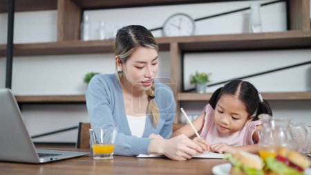 Photo for Asian mother teaching little daughter doing homework at home. Mother helping daughter doing homework. Single mother, Mother and child relationship concept - Royalty Free Image
