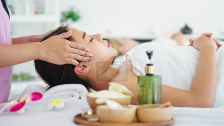 Foto de Hermosa mujer recibiendo masaje en la cabeza en el salón de spa. Mujer acostada en la cama de masaje recibiendo masaje en la cabeza. Cuidado de la salud corporal y masaje tailandés tradicional relajarse - Imagen libre de derechos