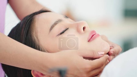 Téléchargez les photos : Gros plan sur le visage de la belle femme asiatique allongée sur un lit de spa relaxant avec un traitement de massage facial. Masseuse massage sur visage de femme. Concept de traitement beauté - en image libre de droit
