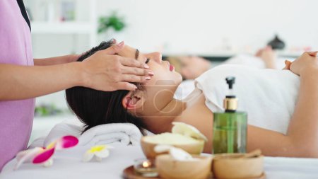 Téléchargez les photos : Belle femme recevant un massage de la tête dans un salon de spa. Femme allongée sur un lit de massage se faisant masser la tête. Soins de santé du corps et massage thaï traditionnel se détendre - en image libre de droit