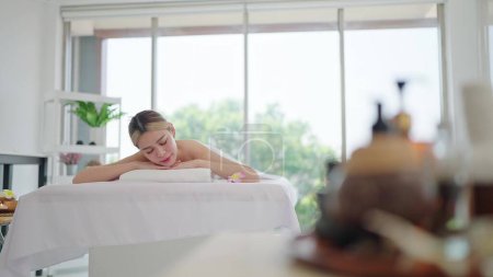 Téléchargez les photos : Belle jeune femme asiatique en serviette couchée sur un lit de spa attendant un traitement spa le week-end au salon de spa. Thérapie, Soins du corps concept - en image libre de droit