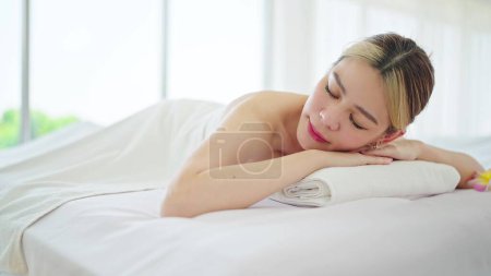 Téléchargez les photos : Gros plan belle jeune femme asiatique allongée sur un lit de spa relaxant en vacances au salon de spa. Femme dormir sur un lit de spa reposant après massage du corps dans un spa station. Soins spa, concept de soins du corps - en image libre de droit