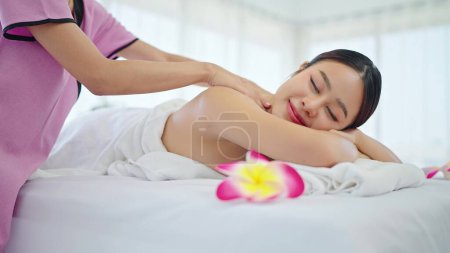 Téléchargez les photos : Thérapeute massant dos de femme asiatique en totwel couché sur le lit relaxant pendant le massage spa. Belle jeune femme asiatique allongée sur un lit de spa et relaxante tout en massant le dos. Concept de relaxation corporelle - en image libre de droit