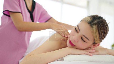 Téléchargez les photos : Belle jeune femme asiatique allongée sur un lit de massage relaxant avec massage du dos au salon de spa. Soins spa, concept de soins du corps - en image libre de droit