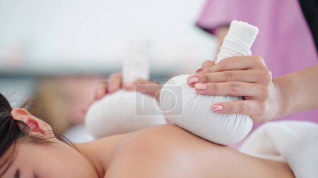 Téléchargez les photos : Gros plan mains de femme masseur à l'aide d'herbes thérapie boule chaude massage retour de la cliente au salon de spa. Thérapie, Massage thaïlandais, Soins du corps concept - en image libre de droit