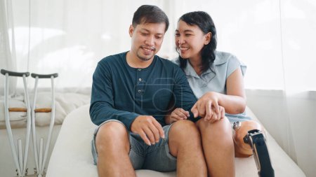 Photo for Happy asian woman in leg prosthesis and her husband sitting on comfortable sofa spending time together at home. Happy asian couple, Leg prosthetic equipment - Royalty Free Image