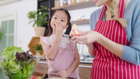 Téléchargez les photos : Bonne petite fille asiatique profiter de manger des pommes dans la salle de cuisine à la maison. Manger des fruits pour les soins de santé. Famille asiatique heureuse, concept d'alimentation saine - en image libre de droit