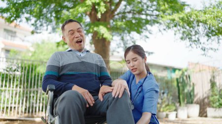 Téléchargez les photos : Asian senior male patient sitting in wheelchair with leg pain. Caregiver nurse take care and support elderly male patient in wheelchair with leg pain - en image libre de droit