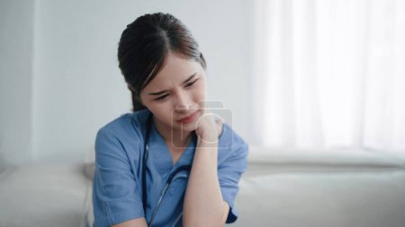 Téléchargez les photos : Jeune infirmière asiatique se sentant fatiguée et déprimée, souffrant de douleurs au cou après avoir travaillé dur. Femme médecin ayant des problèmes de cou et de dos. Épuisement professionnel du médecin - en image libre de droit