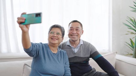 Foto de Feliz anciano asiático pareja tomando selfie mirando smartphone, alegre asiático abuelos teniendo divertido celebración de teléfono hacer instantánea selfie. Pareja mayor tomando selfie en el teléfono celular - Imagen libre de derechos