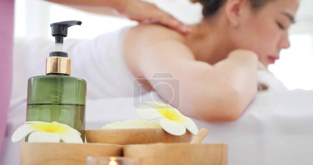 Téléchargez les photos : Fermer les articles et accessoires pour massage. Arrière-plan femme asiatique relaxant avec massage tout en étant couché sur le lit. Bouteille d'huile, fleurs, sucre de gommage ou sel. Centre de bien-être, Healthy Concept - en image libre de droit
