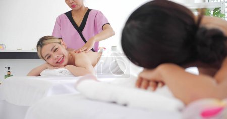 Foto de Dos mujeres asiáticas jóvenes que se relajan con masajes y disfrutan hablando mientras están acostadas en una cómoda cama en el salón de spa. Relajarse en el balneario en vacaciones. Concepto de cuidado corporal - Imagen libre de derechos