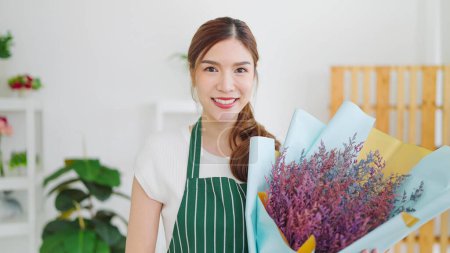 Téléchargez les photos : Portrait de belle femme asiatique appartenant à la boutique de fleurs tenant bouquet de fleurs et souriant à la caméra. Fleuristes femmes tenant bouquet de fleurs debout à la boutique de fleurs. Concept de petite entreprise - en image libre de droit