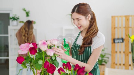 Téléchargez les photos : Belle fleuriste asiatique travaillant avec des fleurs dans un magasin de fleurs. Femme appartenant à la boutique de fleurs coupant des fleurs faisant bouquet pour la vente et la commande de livraison aux clients. Concept de fleuriste - en image libre de droit