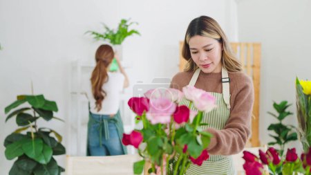 Téléchargez les photos : Jeune fleuriste asiatique en tablier travaillant dans un magasin de fleurs. Fleuriste concentrée jeune femme organisant des fleurs dans la boutique. Concept de petite entreprise - en image libre de droit