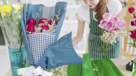 Téléchargez les photos : Fleuriste femme dans tablier travaillant dans un magasin de fleurs. Fleuriste femme créant beau bouquet de fleurs de rose pour la vente et la commande de livraison aux clients. Concept de fleuriste - en image libre de droit