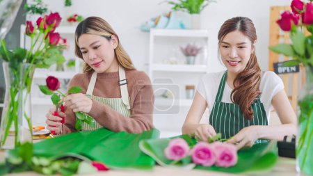 Téléchargez les photos : Deux jeunes fleuristes asiatiques travaillant ensemble dans un magasin de fleurs. Deux collègues femmes parlent et font un beau bouquet de fleurs ensemble à la boutique de fleurs. Concept de fleuriste - en image libre de droit