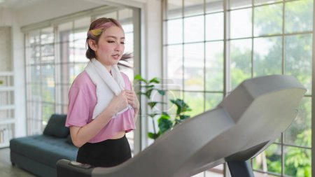 Photo for Young asian women in sportswear with towel around neck exercise on the machine at home. Young women training on elliptical machine. Health care concept - Royalty Free Image