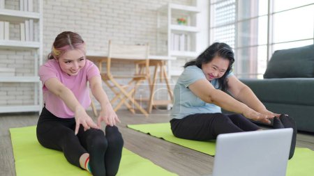Téléchargez les photos : Joyeux jeune fille asiatique et mère âgée regarder tutoriel vidéo exercice formation sur ordinateur portable. Fille et mère âgée aiment s'entraîner ensemble à la maison. Concept d'activité familiale - en image libre de droit